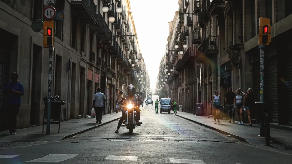 A motorcyclist rides through a sunlit historic street in Barcelona, Spain, capturing urban life.