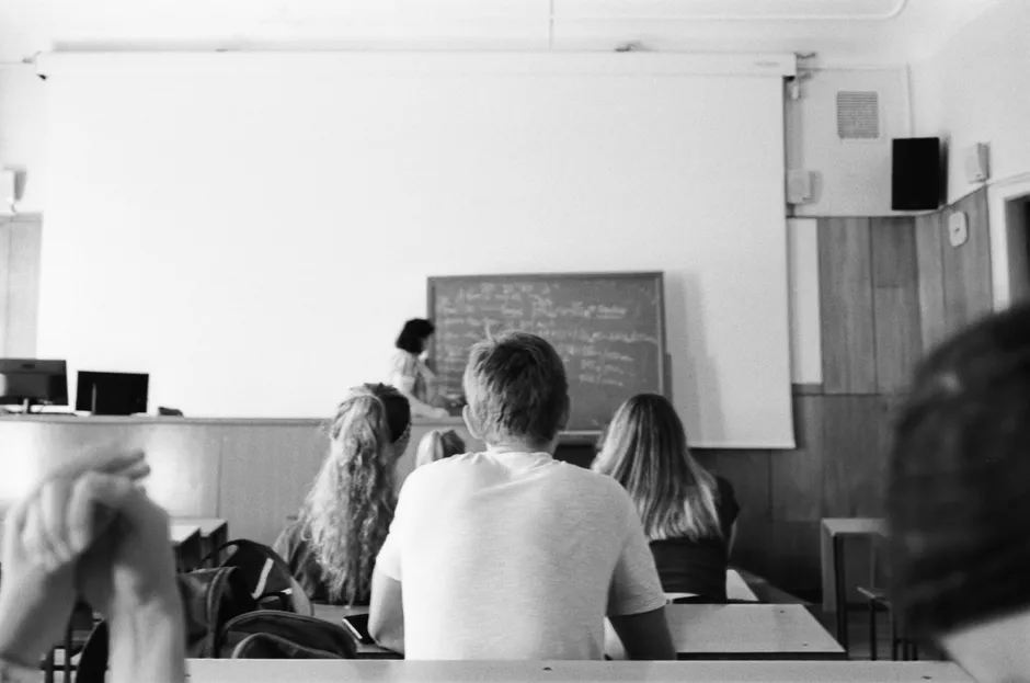 A black and white photo of students and teacher in a classroom setting, focused on learning.