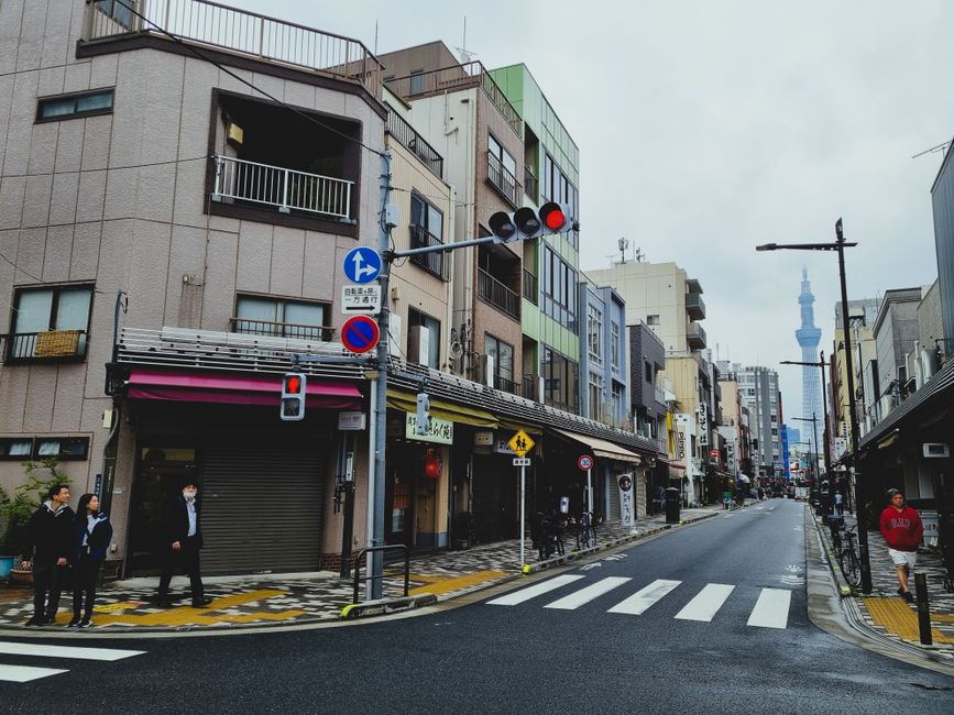 Street scene in Tokyo with pedestrians and the iconic Tokyo Skytree visible in the distance.