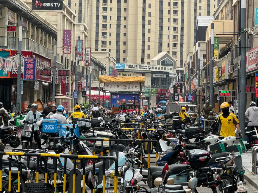 Crowded urban street in Jinnan District, Tianjin, with numerous bikes and pedestrians amidst tall buildings.