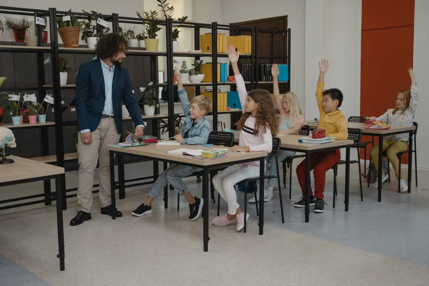 Children actively participating by raising hands during a class session, guided by their teacher.