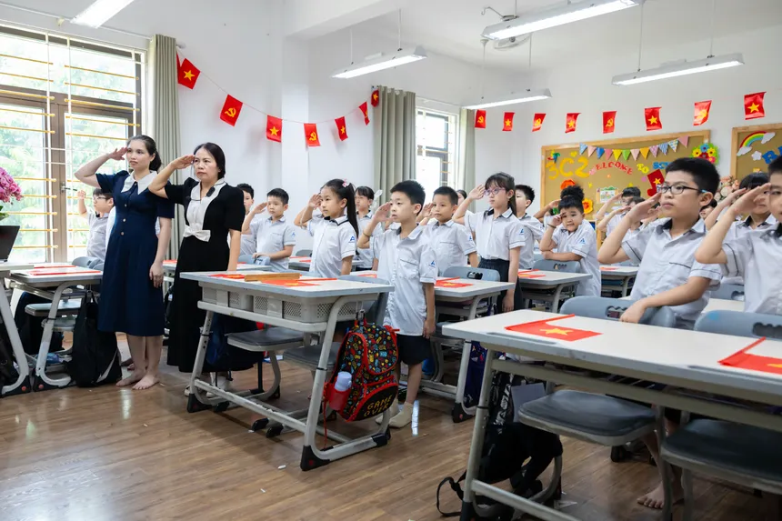 Children and teachers saluting in a colorful classroom decorated with flags.