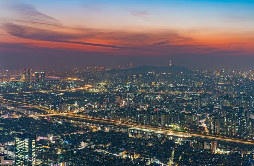 Breathtaking aerial view of illuminated Seoul cityscape at dusk with vibrant sunset sky.